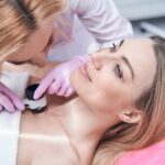 Experienced dermatologist checking moles on skin of young woman